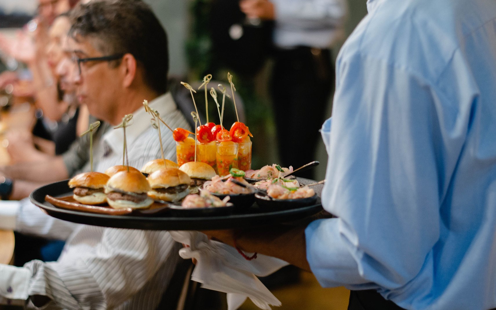 A server carrying a tray of sliders and appetizers at a catered work event