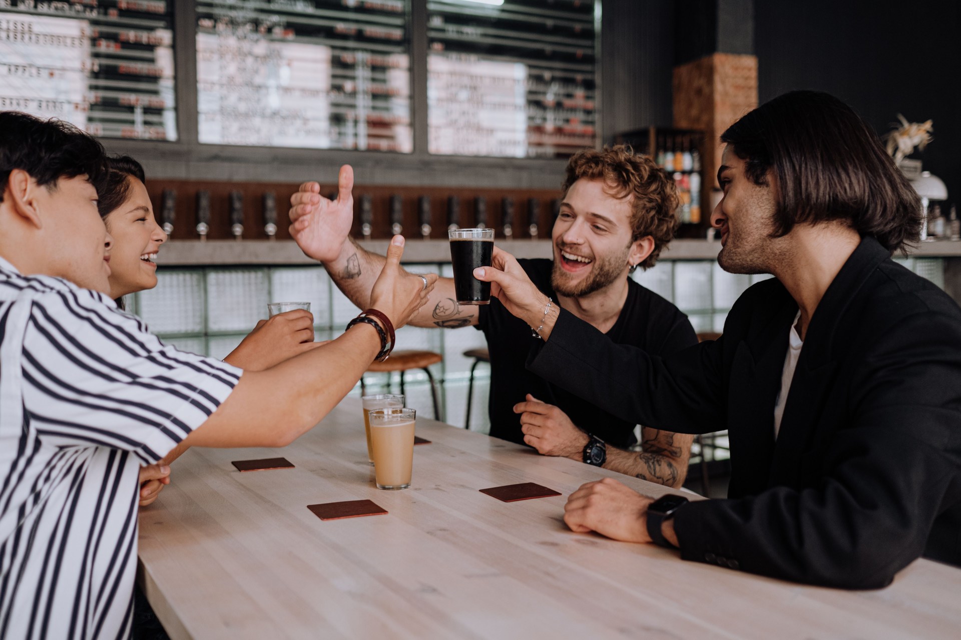 Friends laughing and raising beers together at a brewery taproom