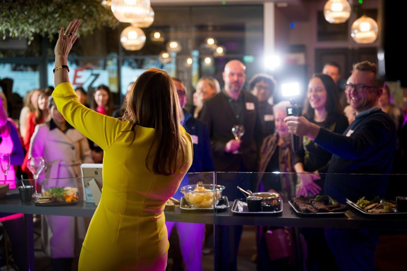 Speaker addressing guests at a corporate networking event with a buffet in a modern venue