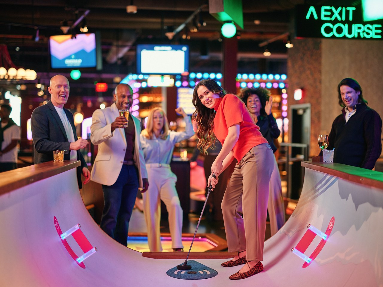 Group of coworkers playing tech-driven mini golf with drinks